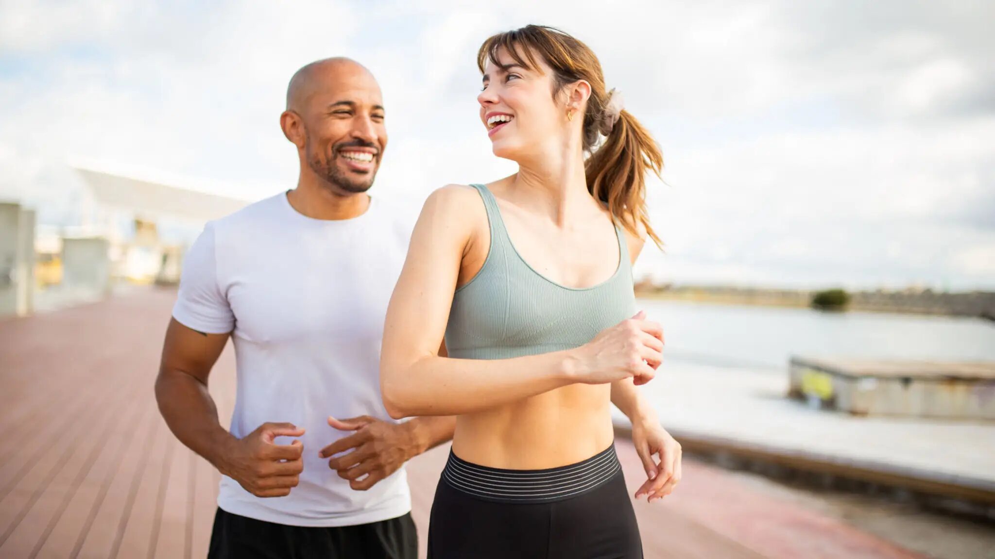 Smiling man and woman jogging on boardwalk