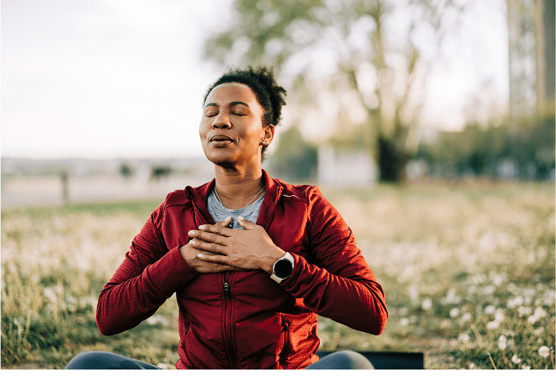 Person meditating outdoors with hands on chest.