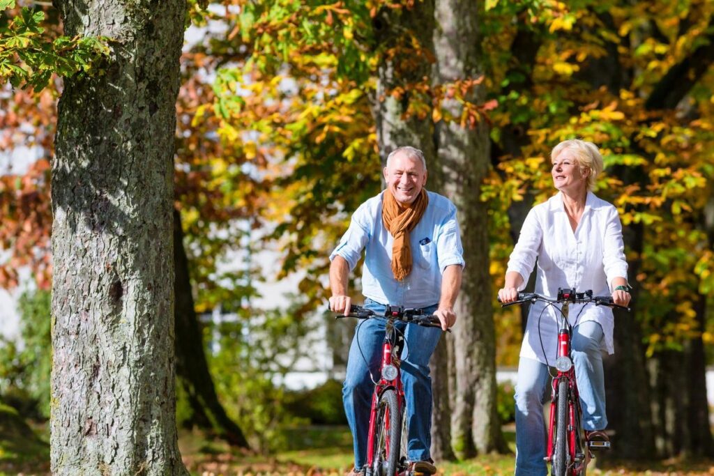 Mature couple biking on autumn tree-lined path