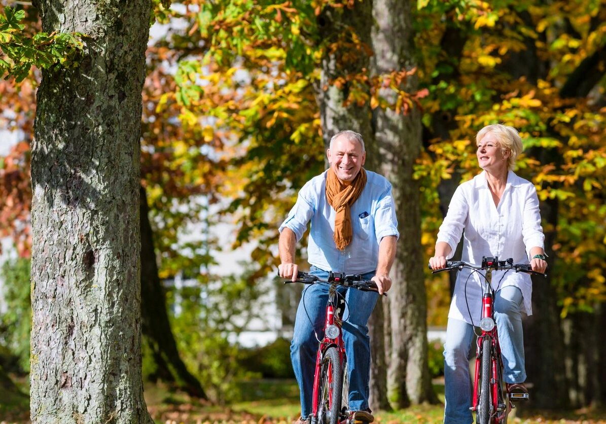 Mature couple biking on autumn tree-lined path