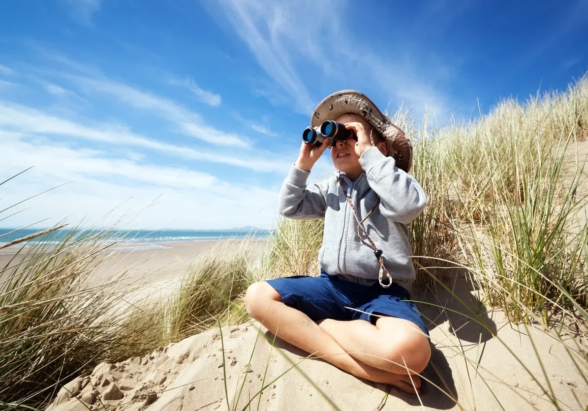 Kid sitting on beach with binoculars